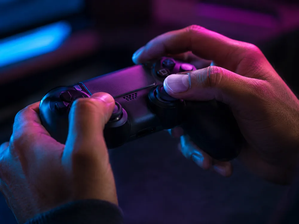 Two hands on a controller at close range, magenta and cyan across the thumbsticks.