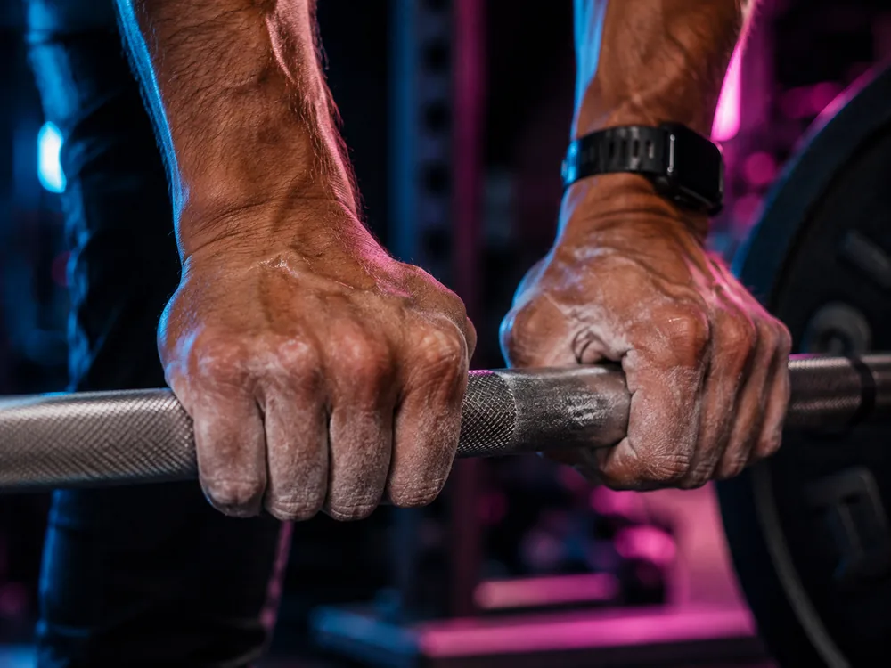 Two chalked hands gripping a loaded barbell, close crop.