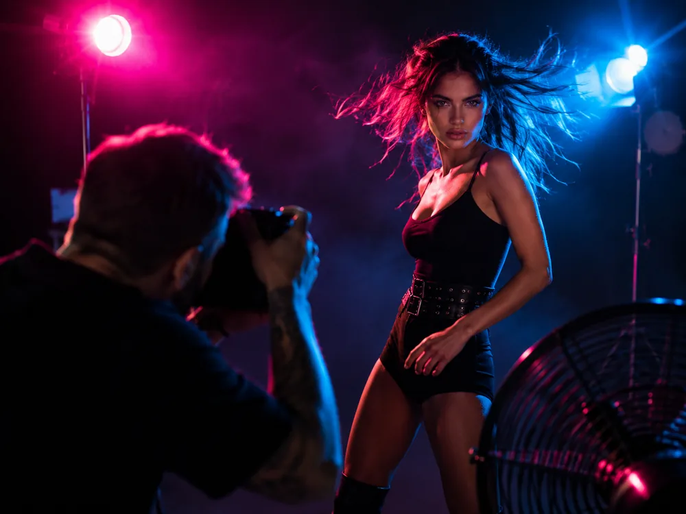 A photographer shooting a model under studio strobes, her hair caught by a wind machine.